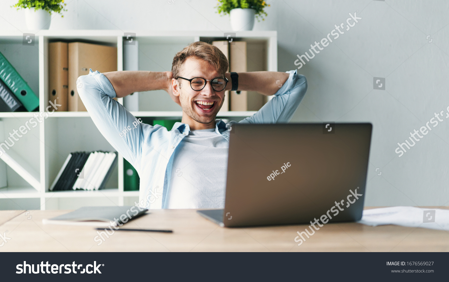 Young man smiling as he reads the screen of a laptop computer while relaxing working on a comfortable place by the wooden table at home. Happy Social distancing #1676569027