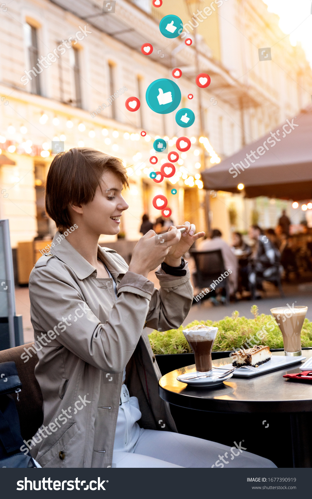 Happy 20s teen girl blogger hold phone take mobile food photo sit at city cafe table get many likes hearts. Young vlogger influencer shoot Instagram stories social media vertical video on smartphone. #1677390919
