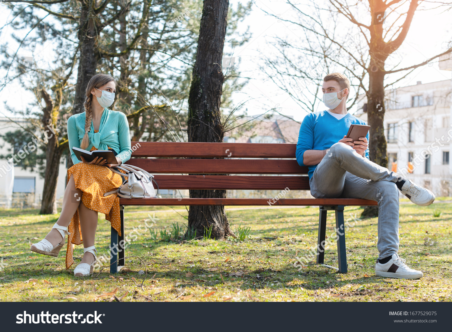 Woman and man in social distancing sitting on bench in park #1677529075