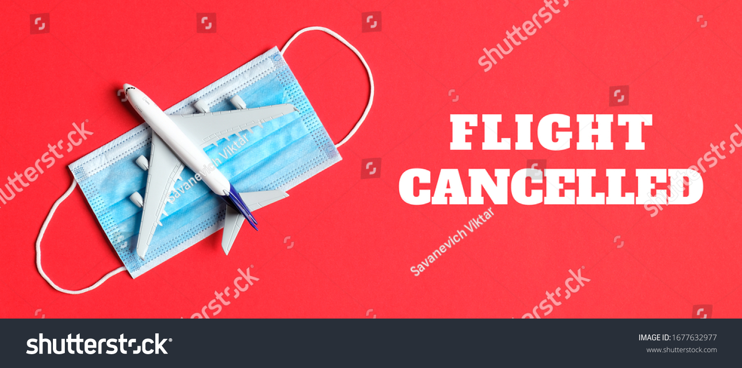 Plane model and face mask on a red background with text flight cancelled. Flight cancellation due to the impact of coronavirus (COVID-19) concept. #1677632977