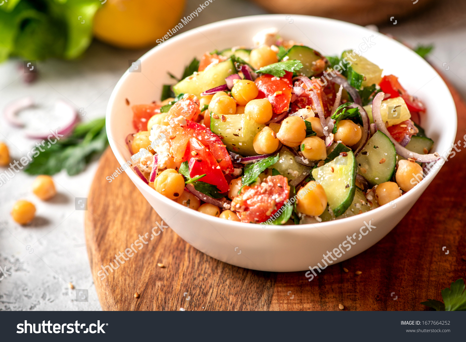Chickpea salad with tomatoes, cucumber, feta cheese, parsley, onions and lemon in a plate on a served table, selective focus. Tasty and healthy vegetarian food, oriental and Mediterranean cuisine. #1677664252
