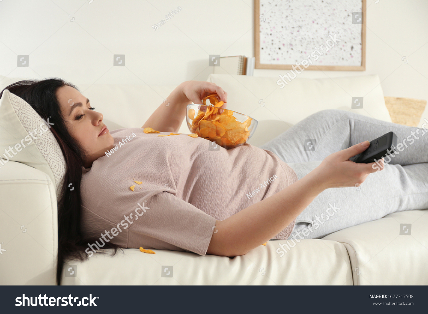 Lazy overweight woman with chips watching TV on sofa at home #1677717508