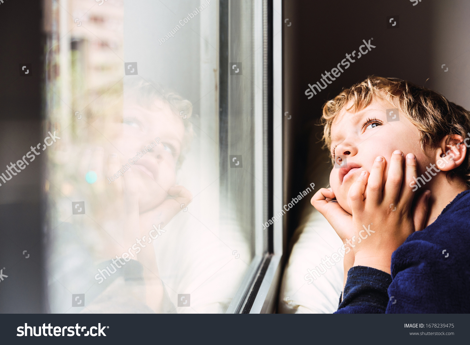 Boy confined at home by the coronavirus crisis in Spain, looks bored out the window without being able to leave home, defocused background. #1678239475
