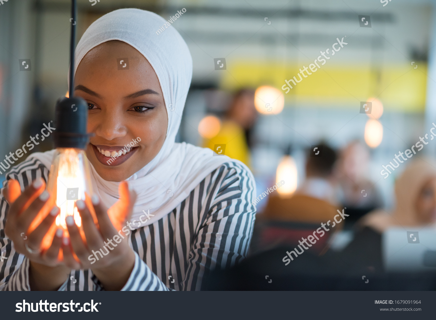 Beautiful african muslim woman holds modern lamp bulb with smiling happy expression, idea concept with selective focus. #1679091964