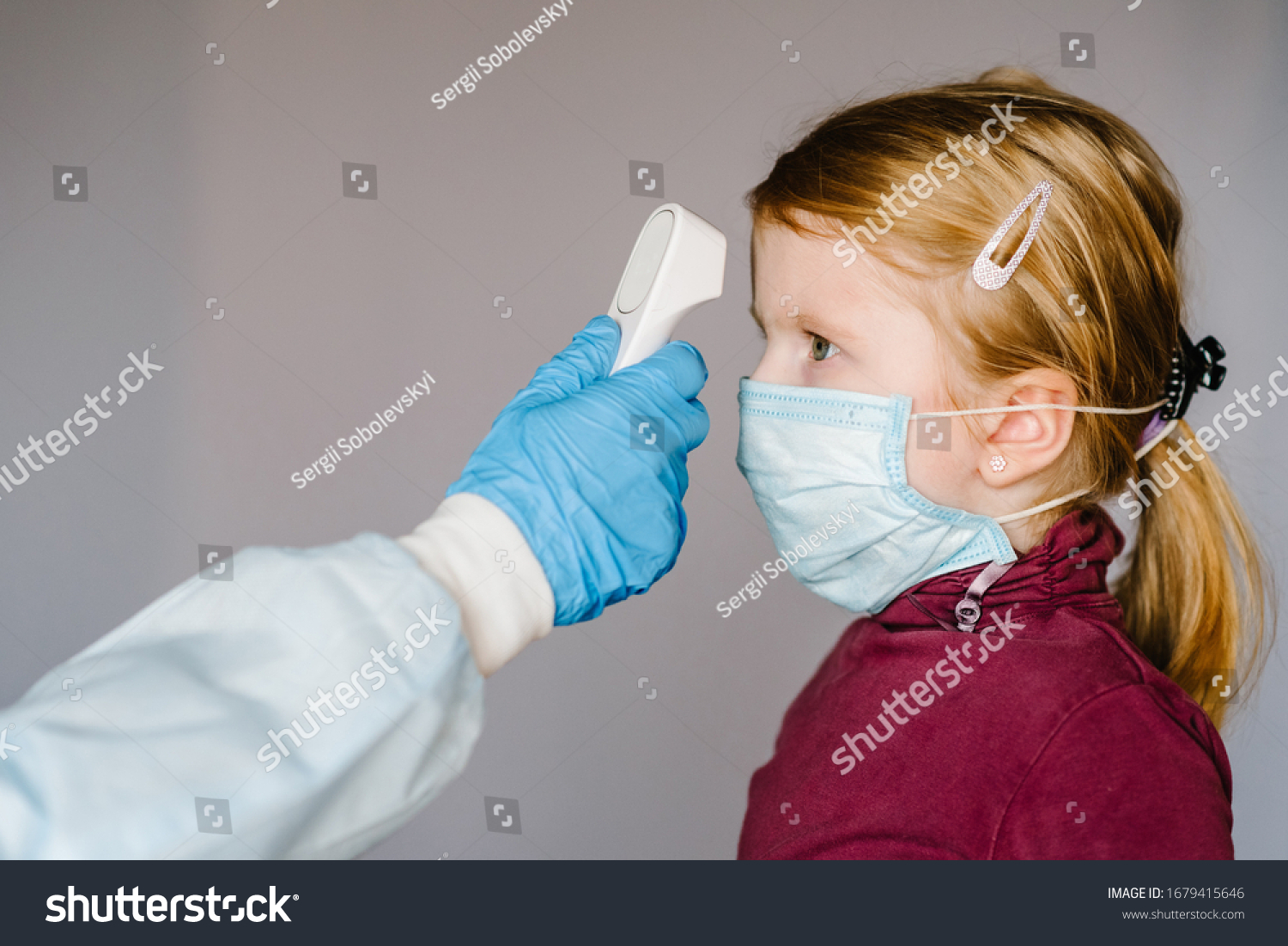 Coronavirus. Nurse or doctor checks girl's body temperature using infrared forehead thermometer (gun) for virus symptom - epidemic outbreak concept. High temperature. #1679415646