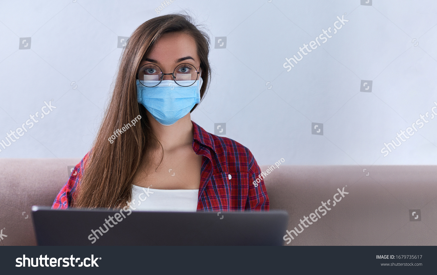 Business woman in round glasses wears medical protective mask working from home at the computer during self-isolation and quarantine. Coronavirus outbreak and covid epidemic. Stay home. Copy space #1679735617