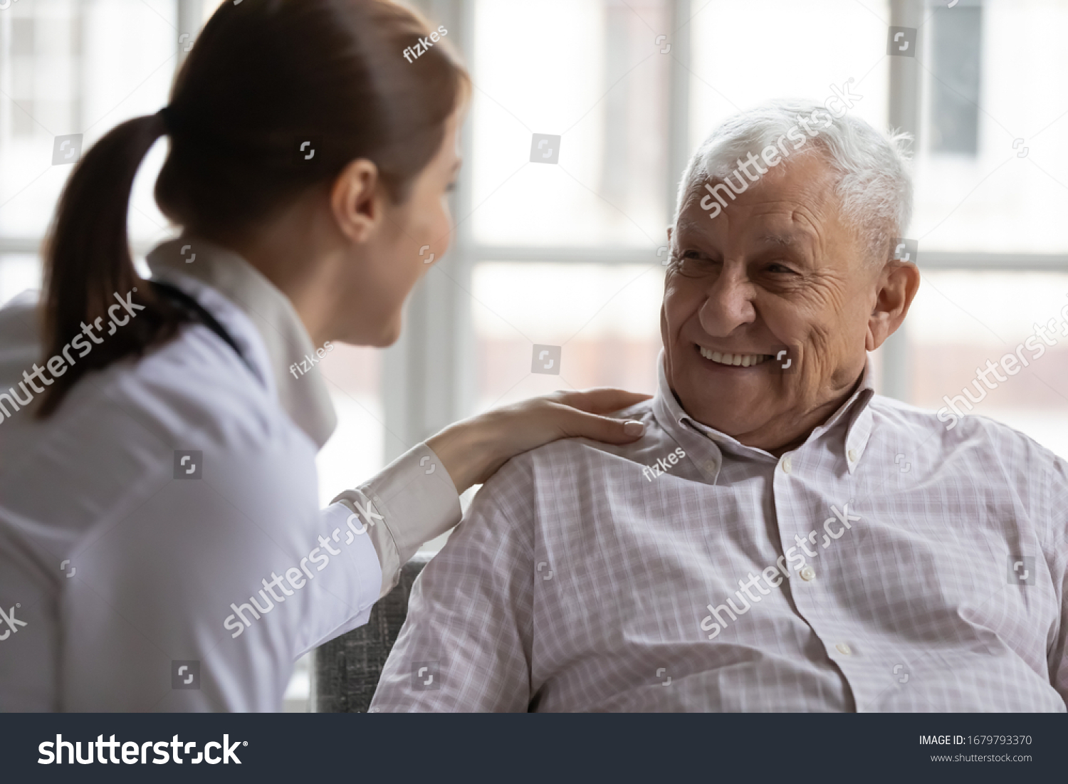 Caring geriatric nurse in white coat cares for grey-haired elderly man in nursing home, listen him relieve solitude, provide support help during visit at home. Homecare eldercare caregiving concept #1679793370