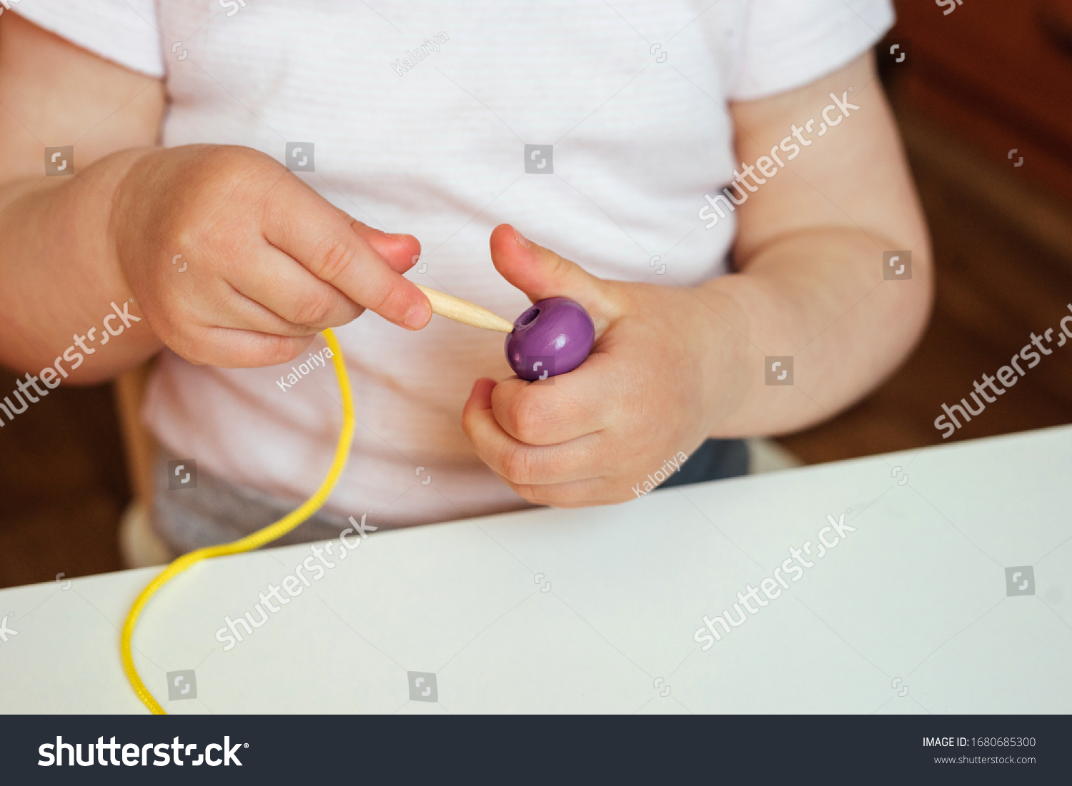 Child putting beads on a string. Bead stringing activity. Fine motor skills development. Early education, Montessori Method. Cognitive skills, children development. Close up of baby's hands. #1680685300