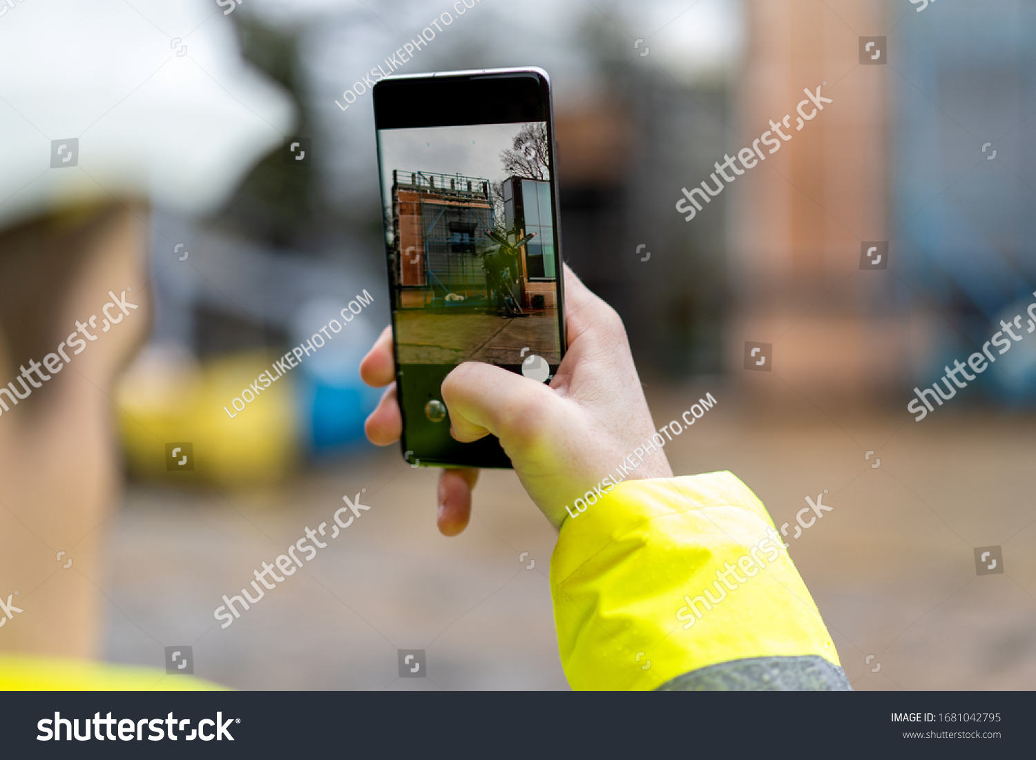 Architect holding a smartphone on construction site. young construction worker is using mobile phone on site. Construction worker with building plans and cellphone. Focus on mobile. warm vivid filter. #1681042795
