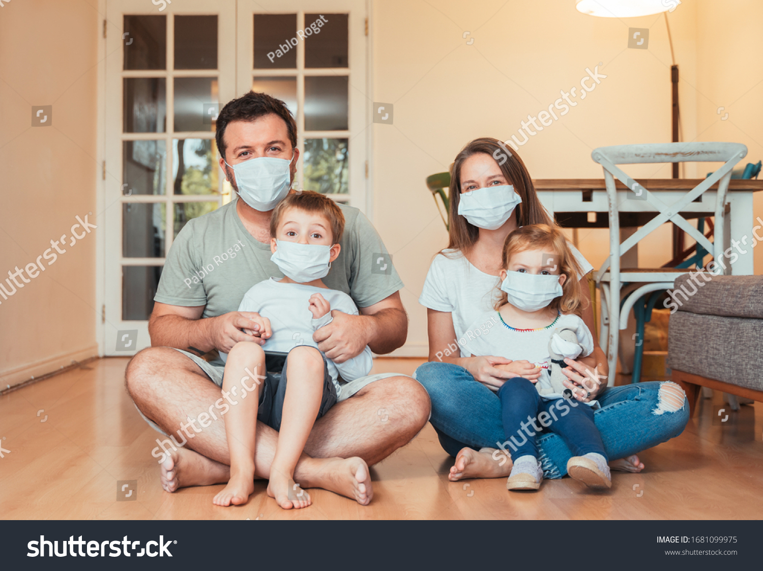 Beautiful young family wearing face masks against coronavirus world pandemic and staying home #1681099975