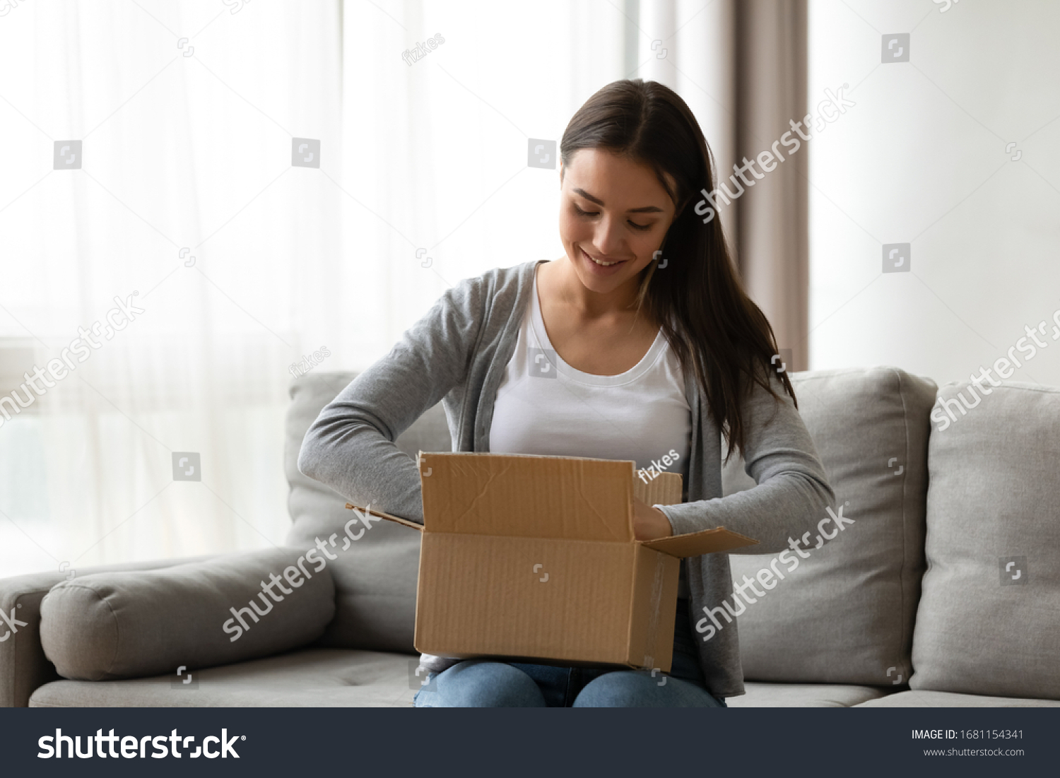 Happy young woman sit on couch in living room unpack cardboard box buying goods on Internet, smiling excited millennial girl open carton parcel order, shopping online, good delivery concept #1681154341