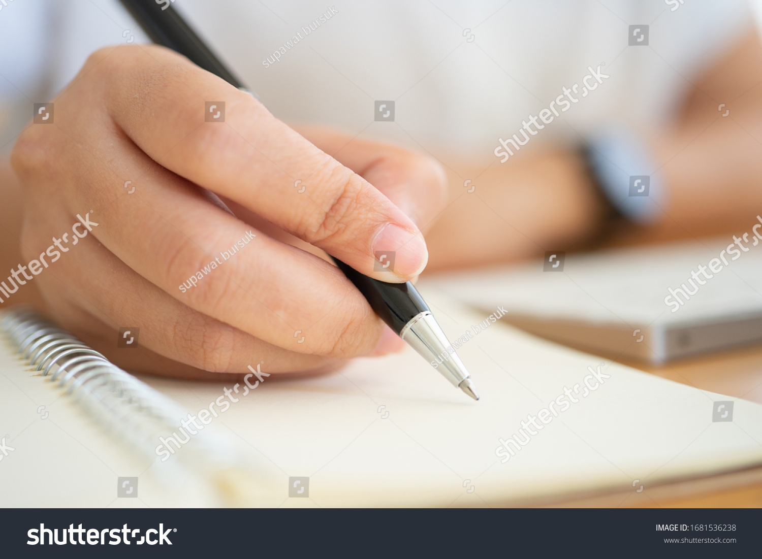 Close shot of businesswoman hands holding a pen writing something on the paper on the foreground in office. Recording concept #1681536238