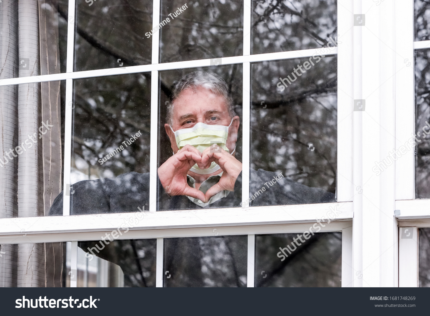 Man wearing mask making heart symbol with hands at the window #1681748269