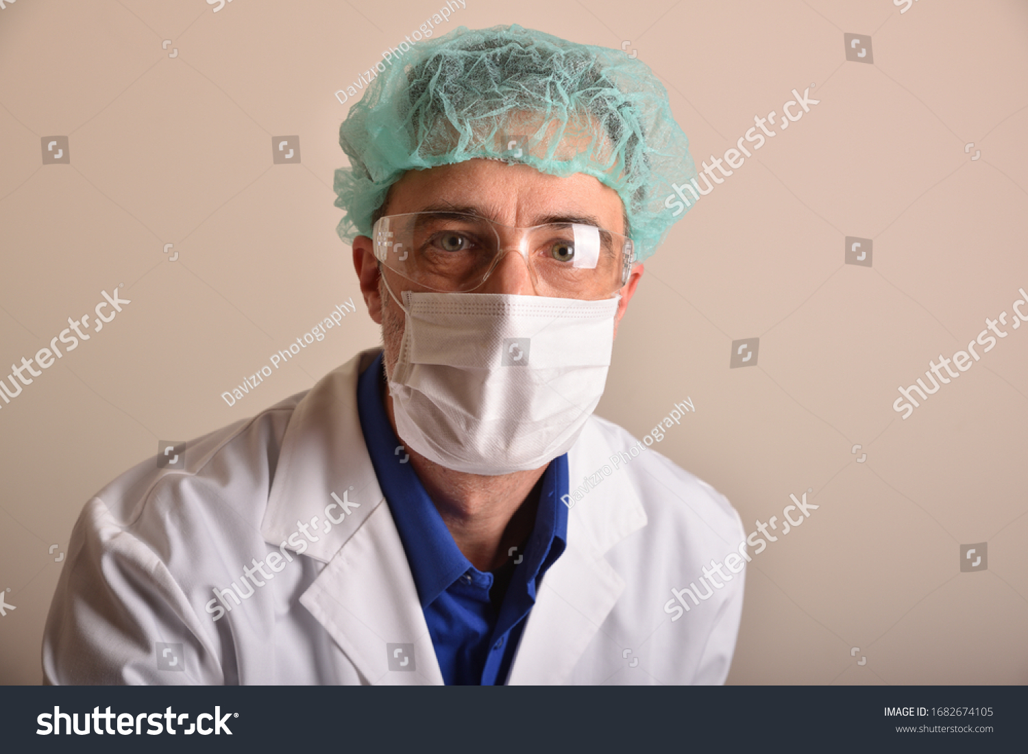 Doctor in his forties with face protection such as a mask, glasses and cap, dressed in a white uniform with a stethoscope hanging from his neck and  brown isolated background. #1682674105
