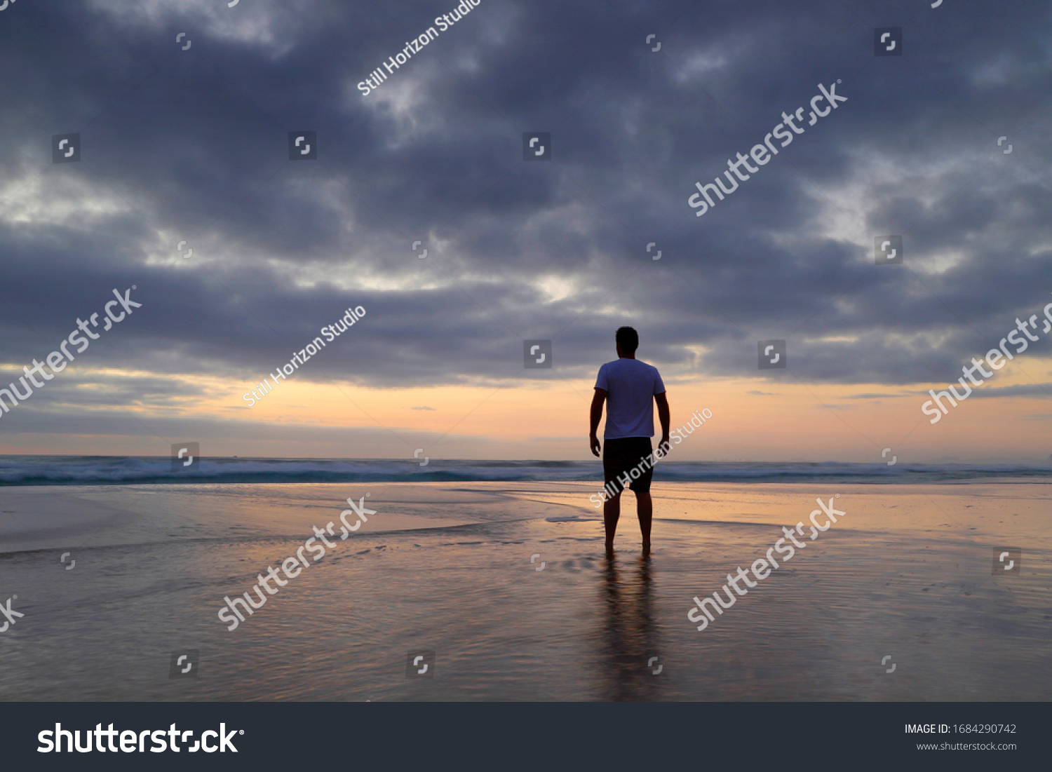 Silhouette of a man standing on the beach on a cloudy morning watching the sunrise. #1684290742