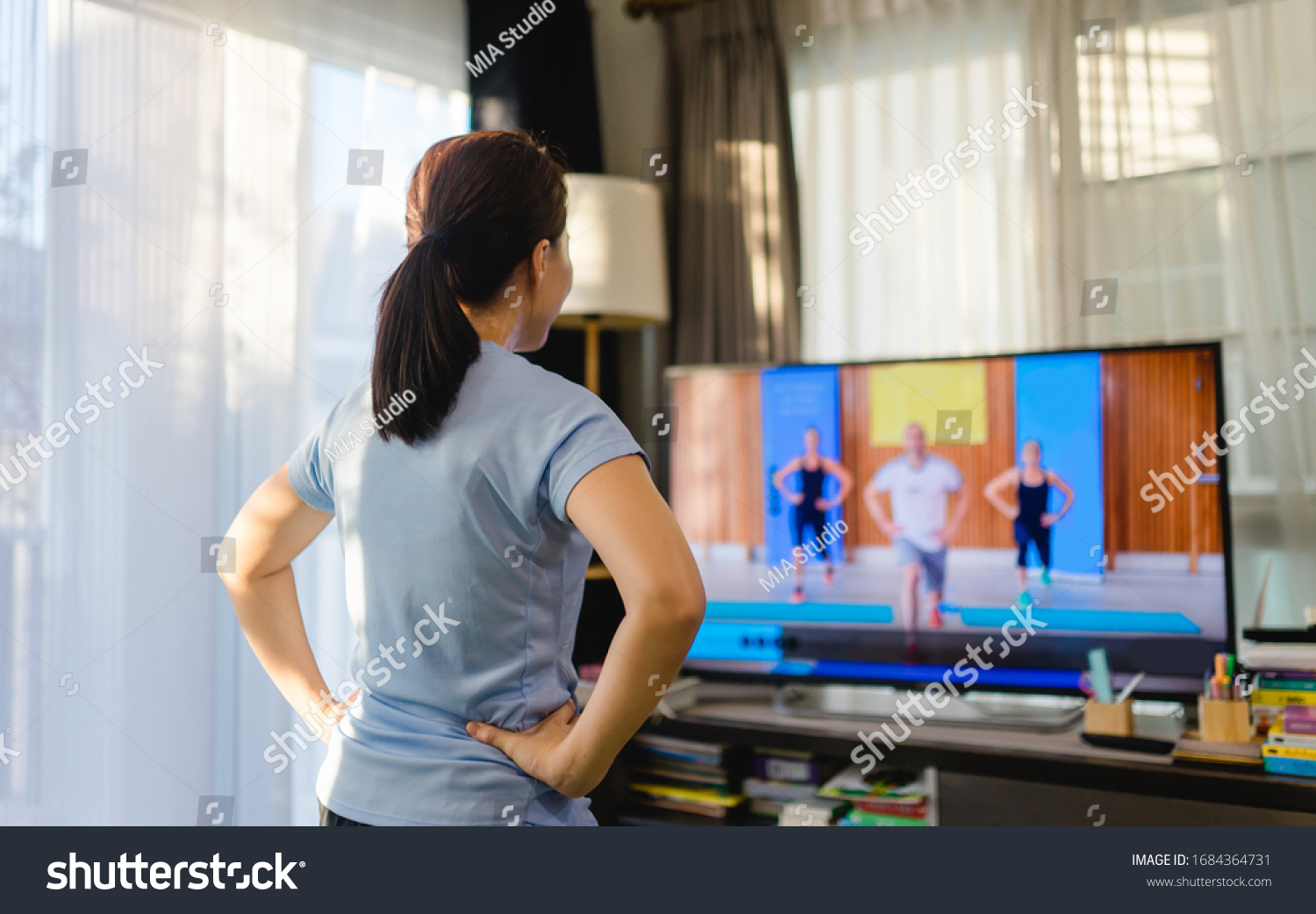 Video streaming Stay home.home fitness workout class live streaming online.Asian woman doing strength training cardio aerobic dance exercises watching videos on a smart tv in the living room at home.
