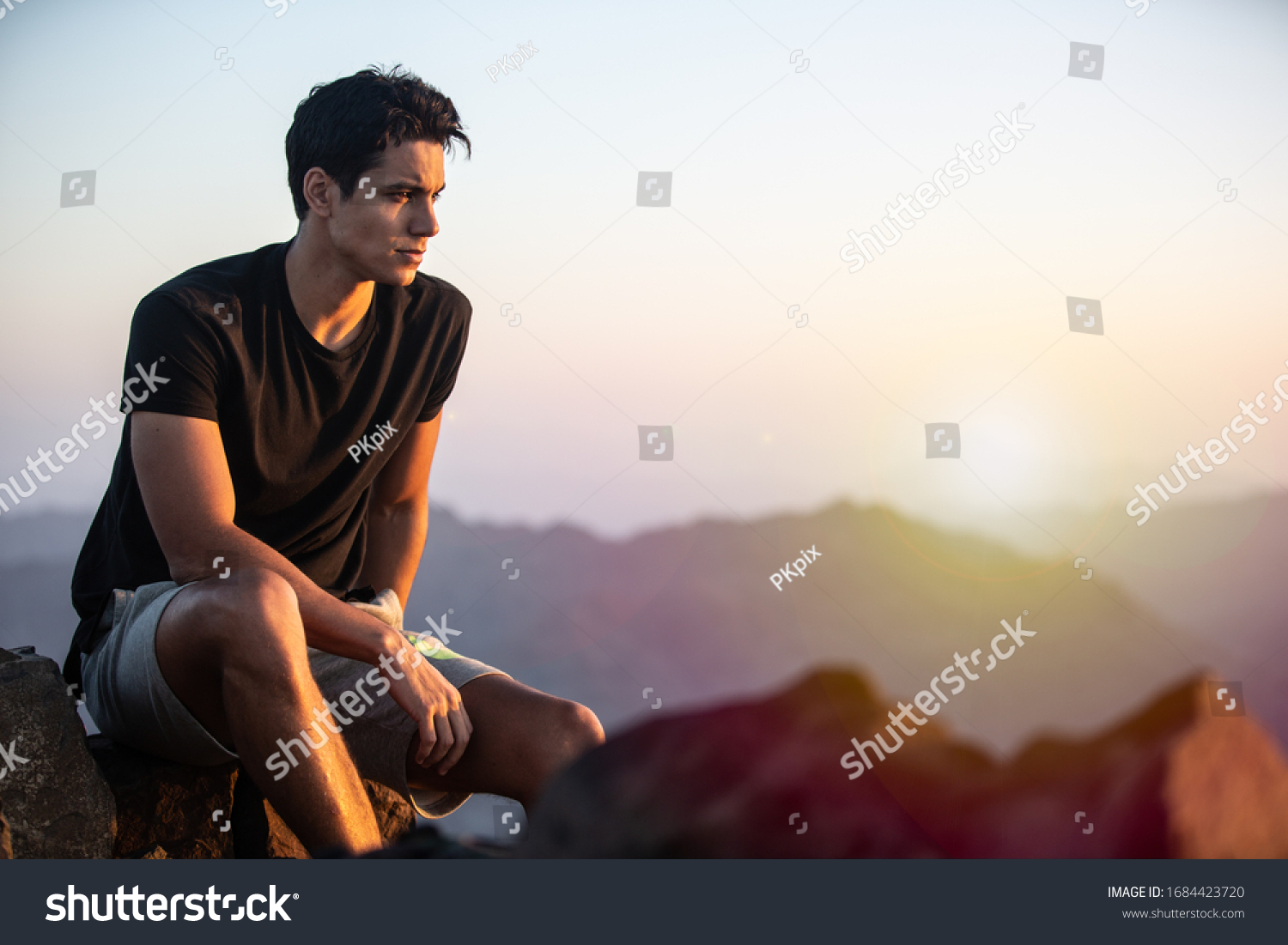 Handsome young man sitting on top of a mountain at beautiful sunset.  #1684423720