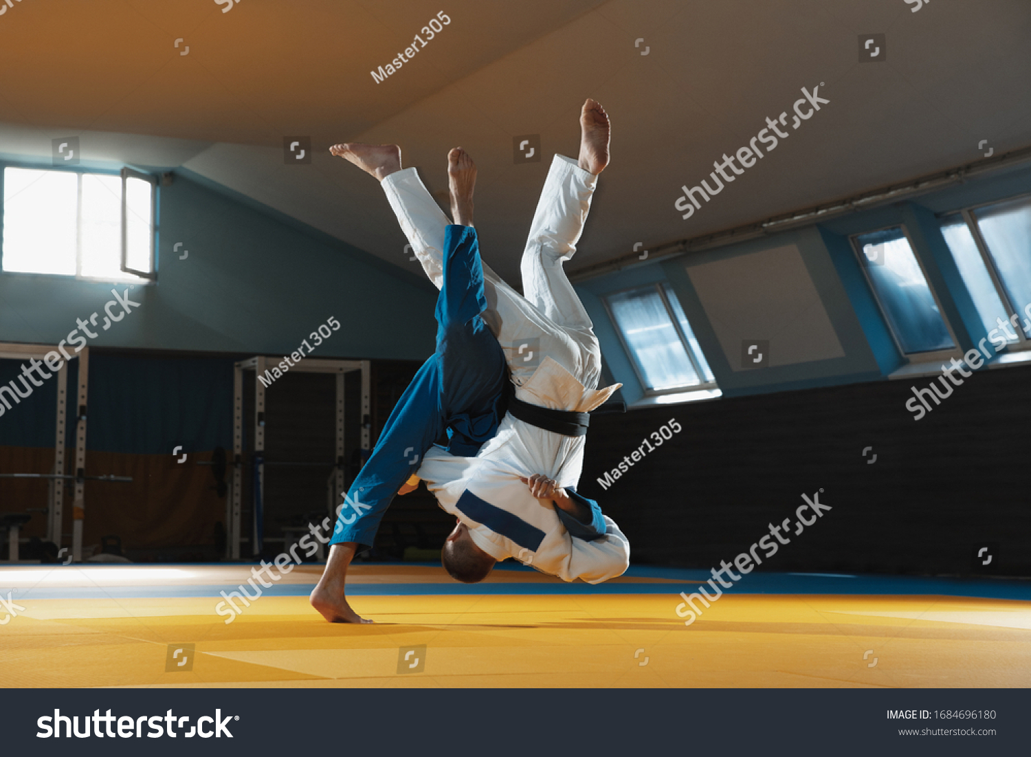 Two young judo caucasian fighters in white and blue kimono with black belts training martial arts in the gym with expression, in action, motion. Practicing fighting skills. Overcoming, reaching target #1684696180