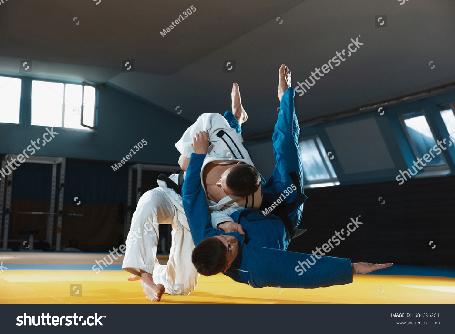 Two young judo caucasian fighters in white and blue kimono with black belts training martial arts in the gym with expression, in action, motion. Practicing fighting skills. Overcoming, reaching target #1684696264