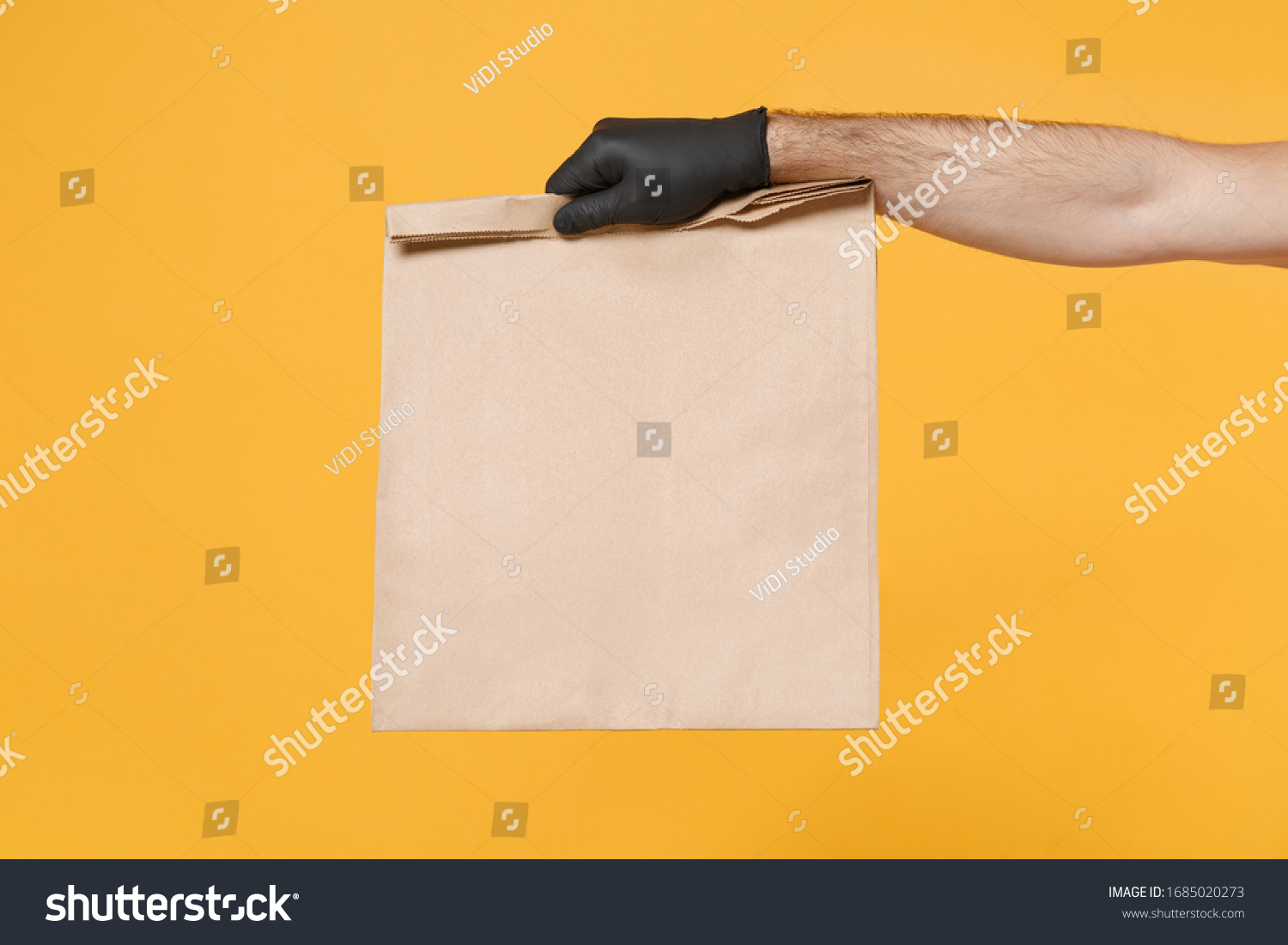 Close up male hold in hand glove brown clear empty blank craft paper bag for takeaway isolated on yellow background. Packaging template mockup. Delivery service concept. Copy space Advertising area #1685020273