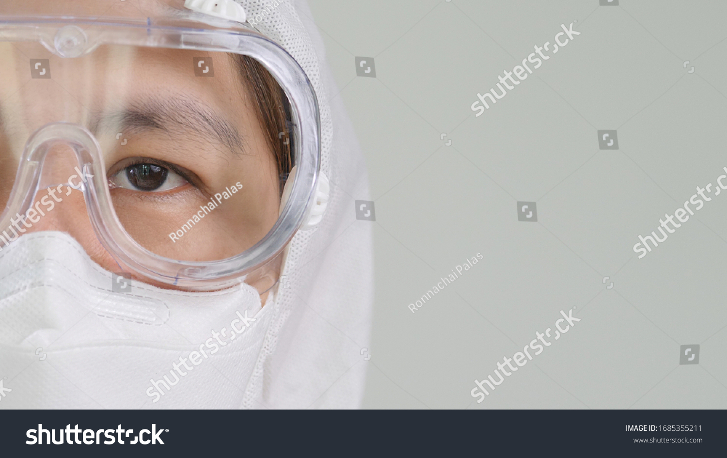 Close up open eye of Asian doctor in protective hazmat PPE suit wearing face mask and eyeglasses with copy space #1685355211