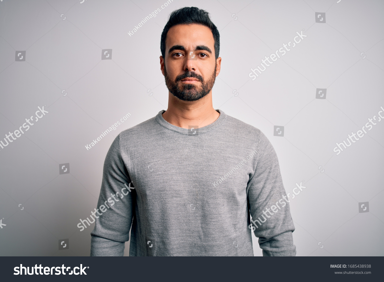 Young handsome man with beard wearing casual sweater standing over white background Relaxed with serious expression on face. Simple and natural looking at the camera. #1685438938