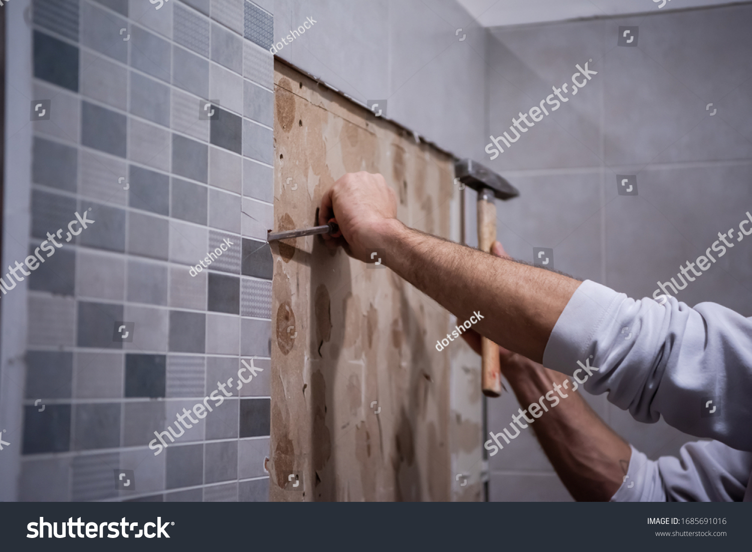 professional worker remove demolish old tiles in a bathroom with hammer and chisel #1685691016