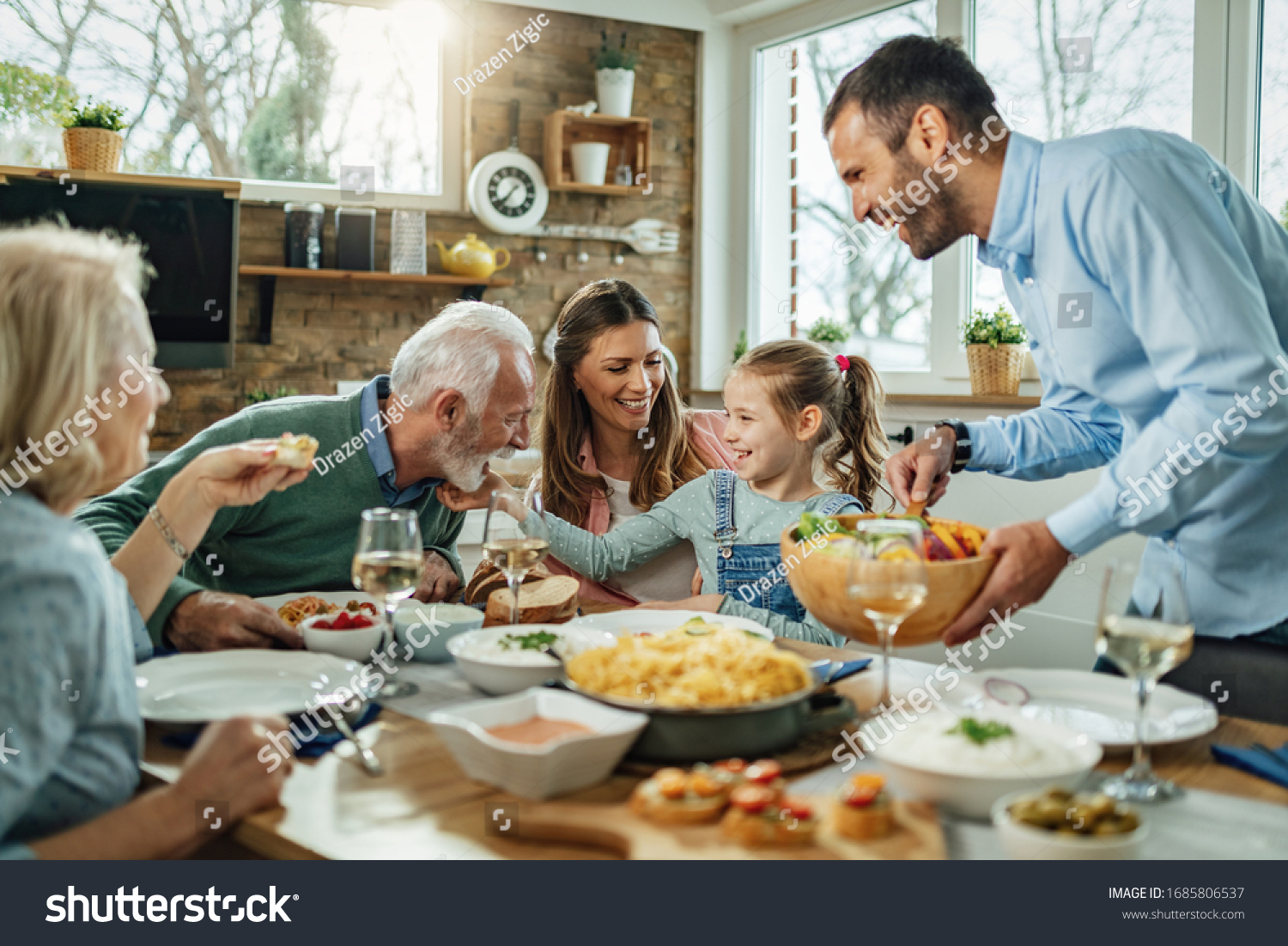 Happy multi-generation family gathering around dining table and having fun during a lunch.  #1685806537