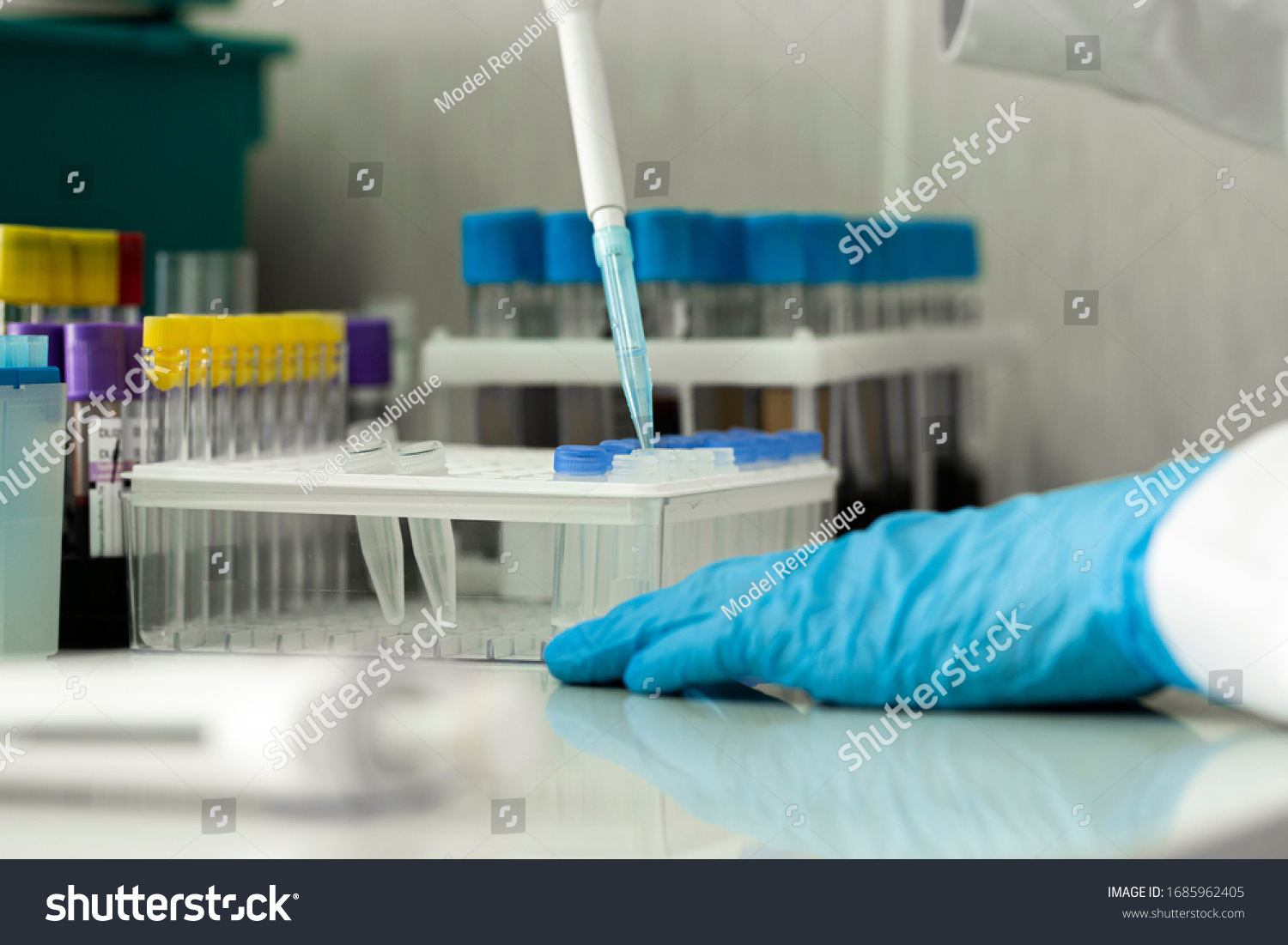 Close-up shoot of scientist lab technician assistant in rubber gloves working with samples in laboratory adding fluid to one of several test tubes with pipette. Covid-19 vaccine reserch concept #1685962405
