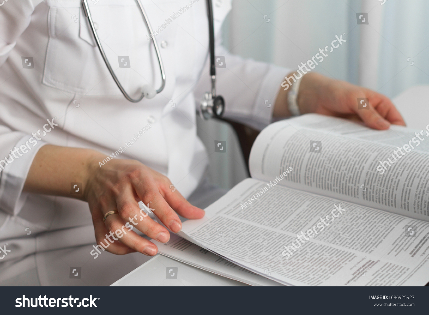 Hands of a female doctor holding a  medical journal in diagnostic cabinet. Doctor is waiting for patient. Stethoscope. Coronavirus. #1686925927