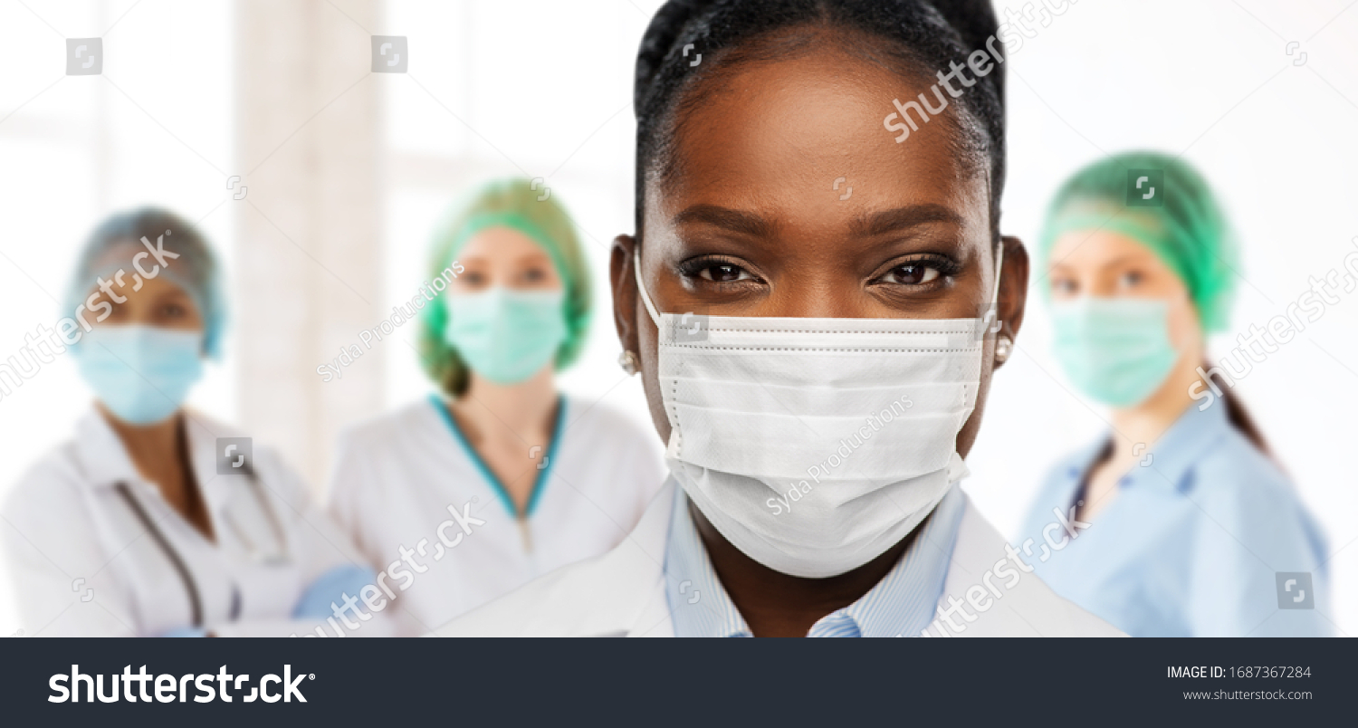health, medicine and pandemic concept - close up of african american female doctor or scientist in protective mask over medical workers at hospital on background