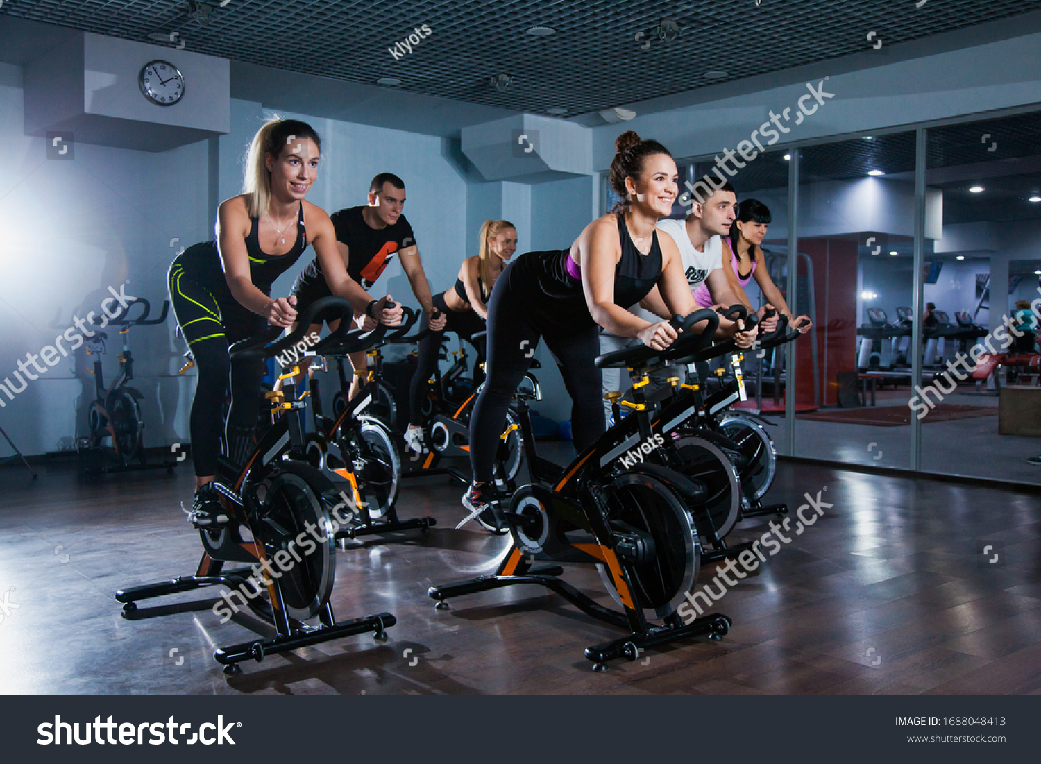 Cycling class in fitness club, group of fit people spinning on cardio machine. Man and women do sports exercises at gym fat burning class. Active lifestyle, health care and body training concept #1688048413