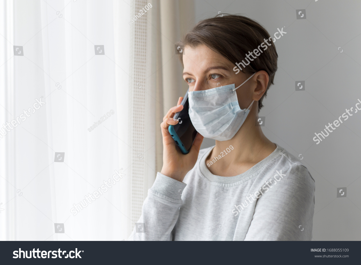 A young woman in a medical mask in quarantine is talking on the phone. outbreak concept #1688055109