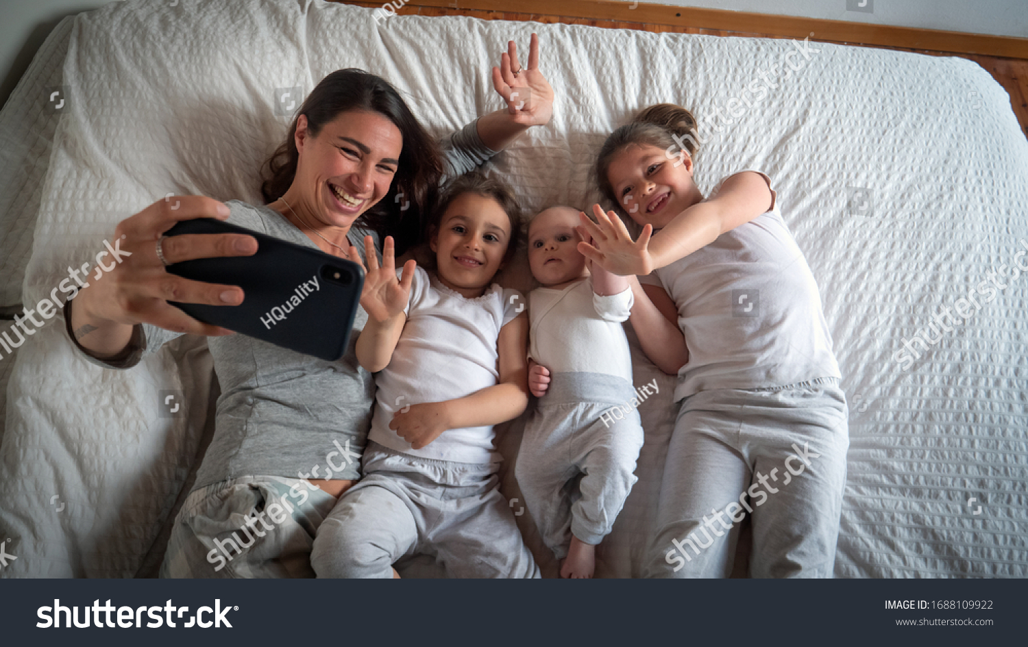 Authentic shot of happy mother with her kids are making a selfie or video call to father or relatives in a bed. Concept of technology, new generation,family, connection, parenthood, authenticity #1688109922