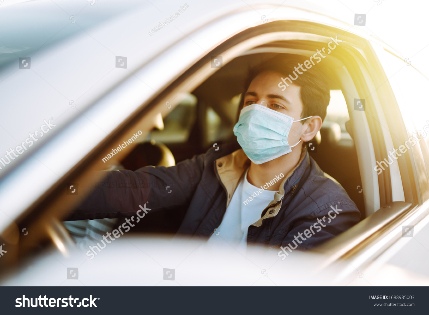 Young man in protective sterile medical mask driving car. The concept of preventing the spread of the epidemic and treating coronavirus, pandemic in quarantine city. Covid -19. #1688935003