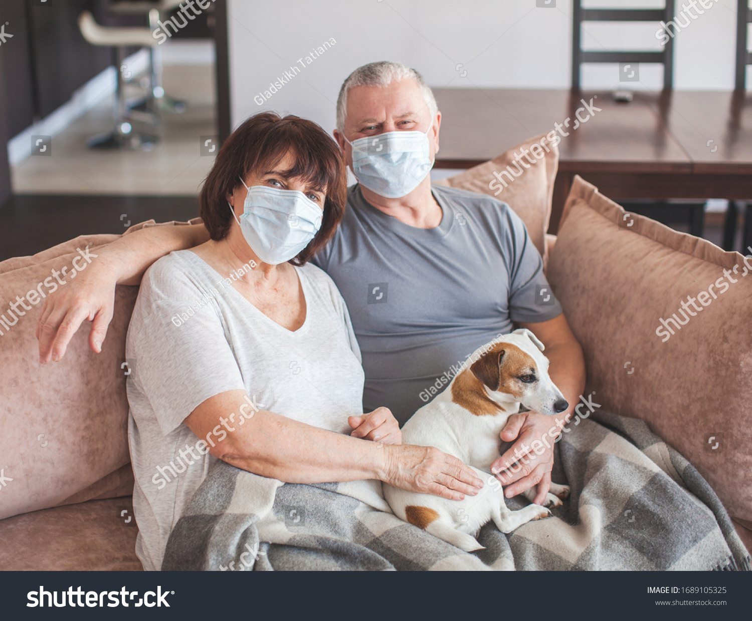 Coronavirus CoVid-19 Couple old aged senior people at home with seasonal winter cold illness disease sit down on the sofa. Elderly couple in medical masks during the pandemic #1689105325