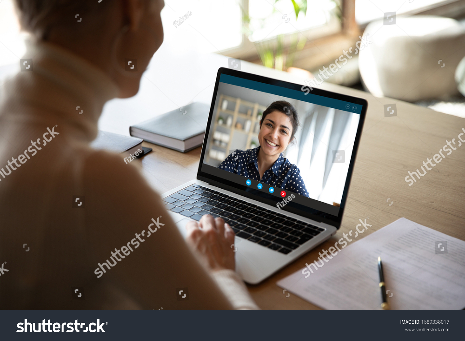 Young female sit at desk at home talk on video call with Indian colleague, woman have pleasant Webcam conference with biracial coworker, communicate online using wireless Internet connection #1689338017