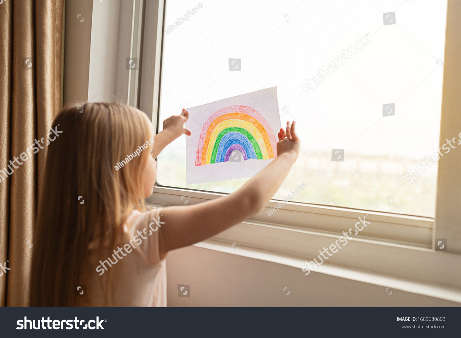 Kid painting rainbow during Covid-19 quarantine at home. Girl near window. Stay at home Social media campaign for coronavirus prevention, let's all be well, hope during coronavirus pandemic concept #1689680803