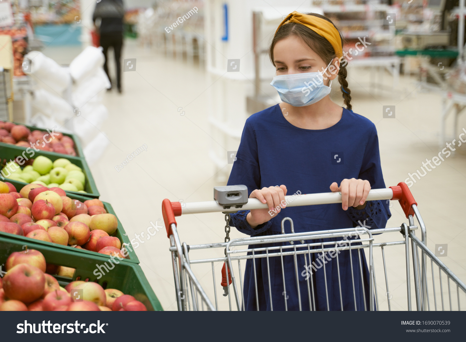 Girl in disposable medical mask shopping in supermarket during an outbreak of coronavirus pneumonia, makes panic stock of products. Empty store shelves, set of products for quarantine self-isolation #1690070539
