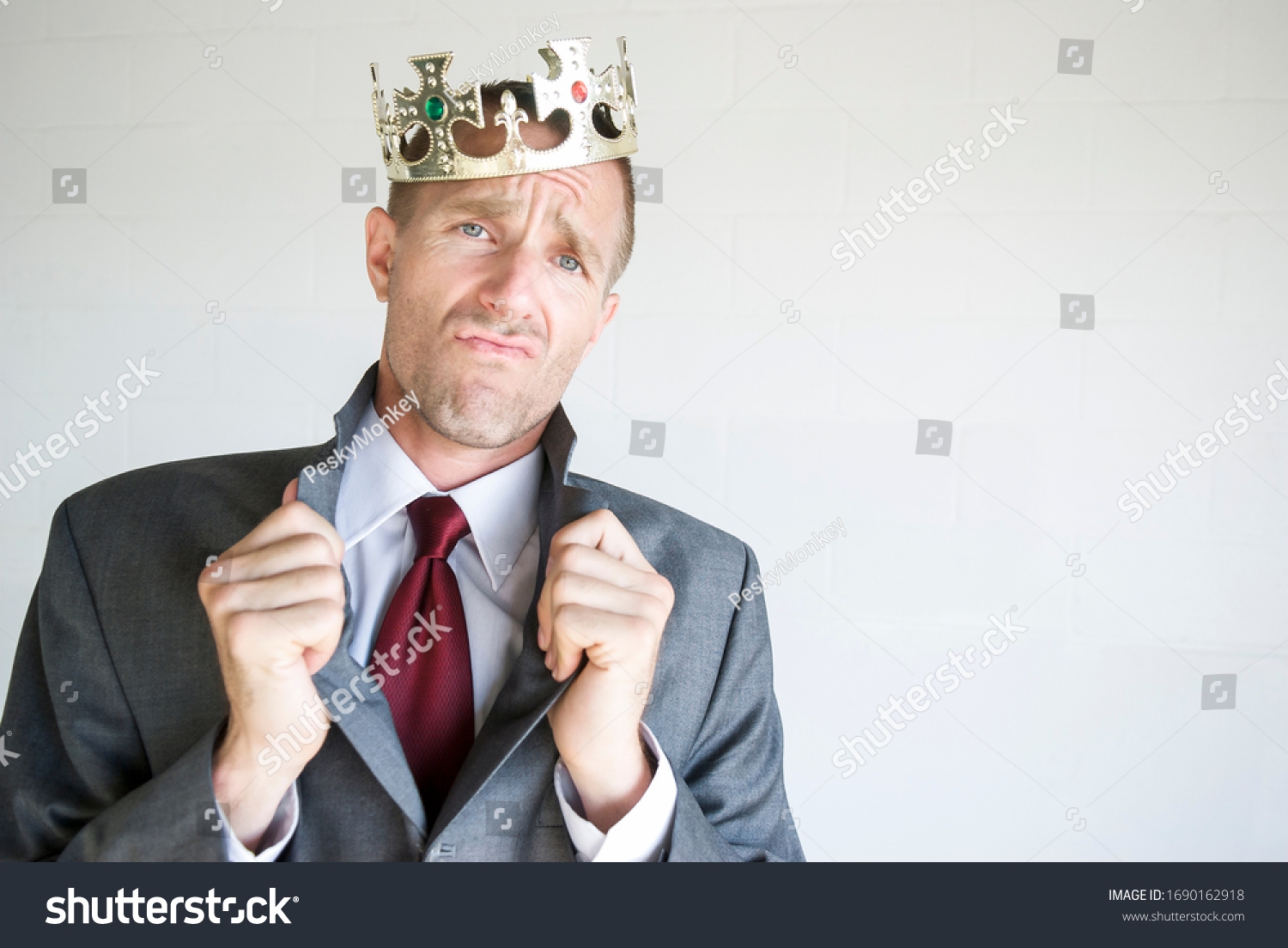 Cocky businessman wearing golden jeweled crown popping his collar with an arrogant expression #1690162918
