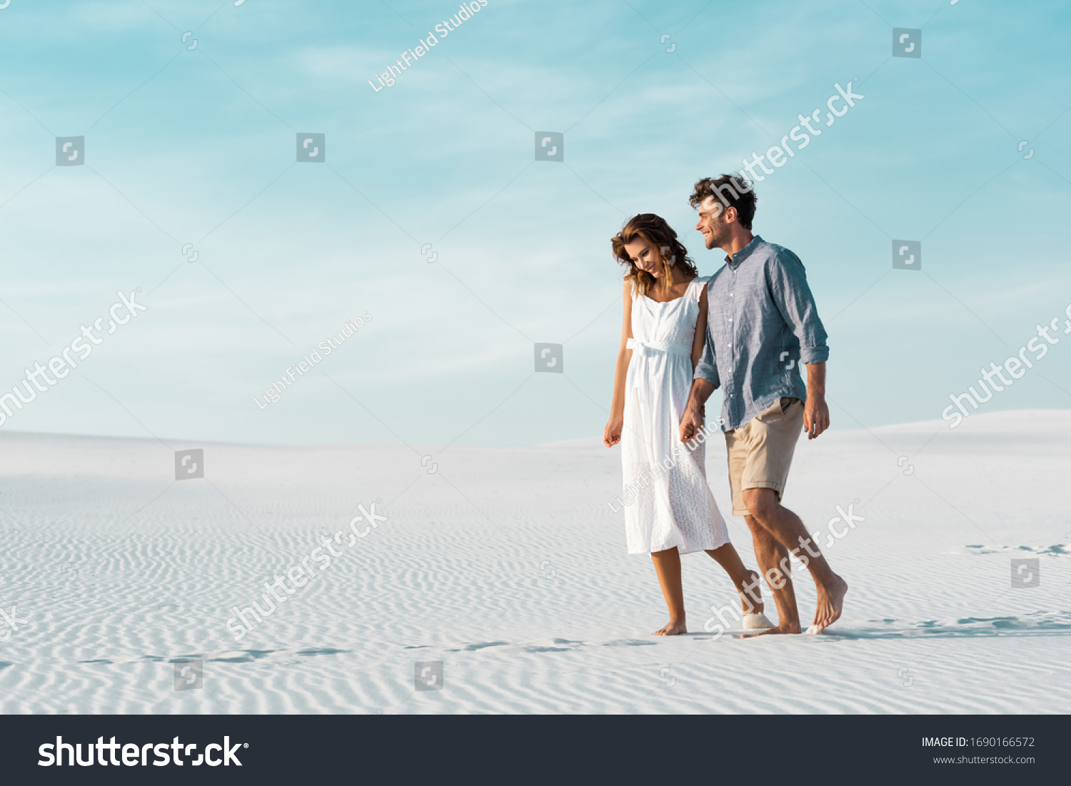 young couple walking on sandy beach against blue sky #1690166572