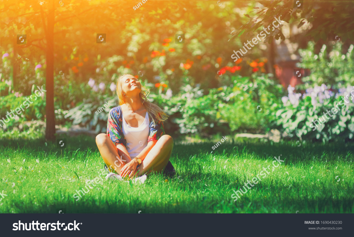 Happy free young woman sitting outdoors in yoga position with closed eyes on summer park grass Calm girl enjoy smile and relax in spring city air. Mindset inner light peace concept.  #1690430230