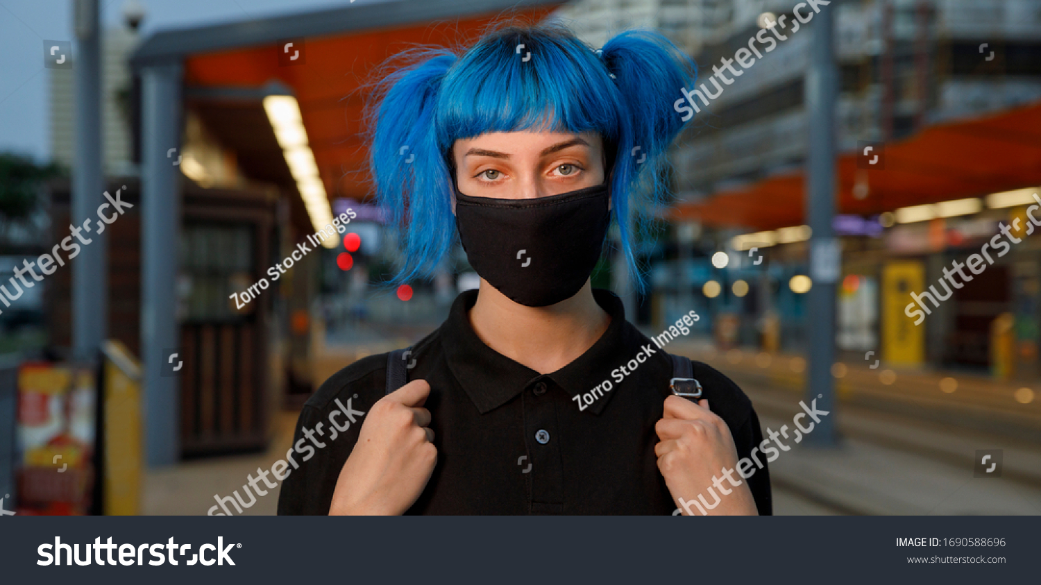 coronavirus fashionable medical face mask worn by young female student with blue anime style hair at tram stop on city street on dusk, stop covid 19 pandemic or air pollution concept, panorama banner #1690588696