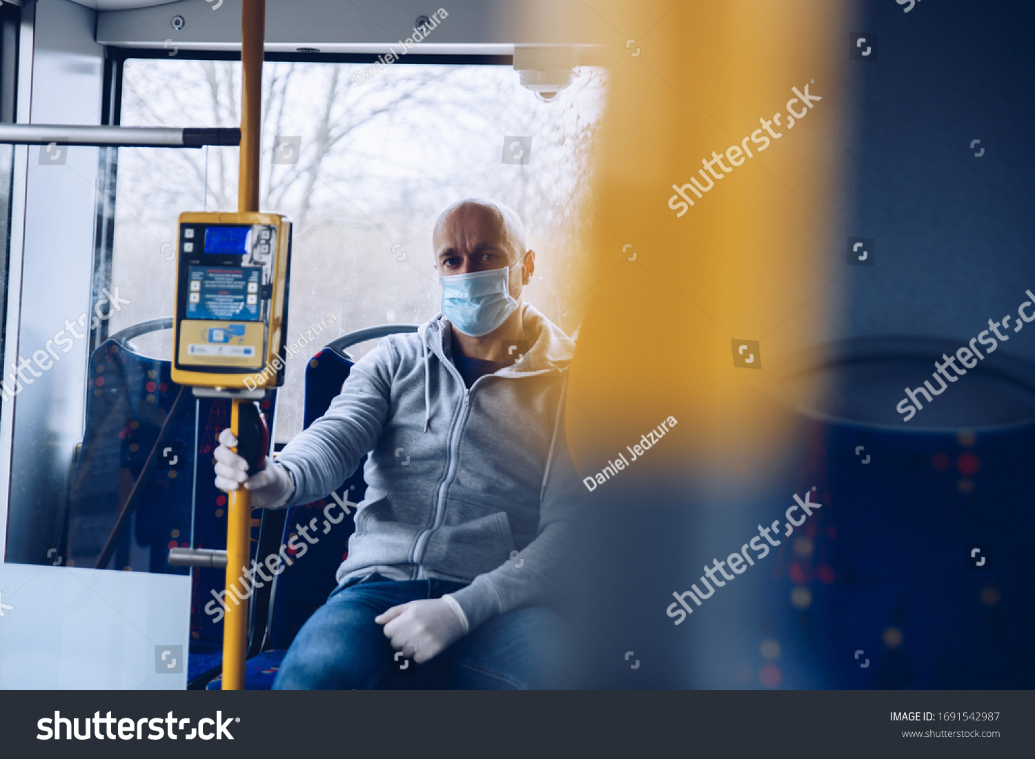Man in mask and protective gloves traveling by city bus during coronovirus covid-19 pandemic #1691542987