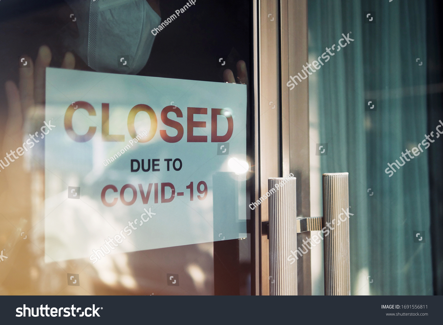Business office or store shop is closed, bankrupt business due to the effect of novel Coronavirus (COVID-19) pandemic. Unidentified person wearing mask hanging closed sign in background on front door. #1691556811