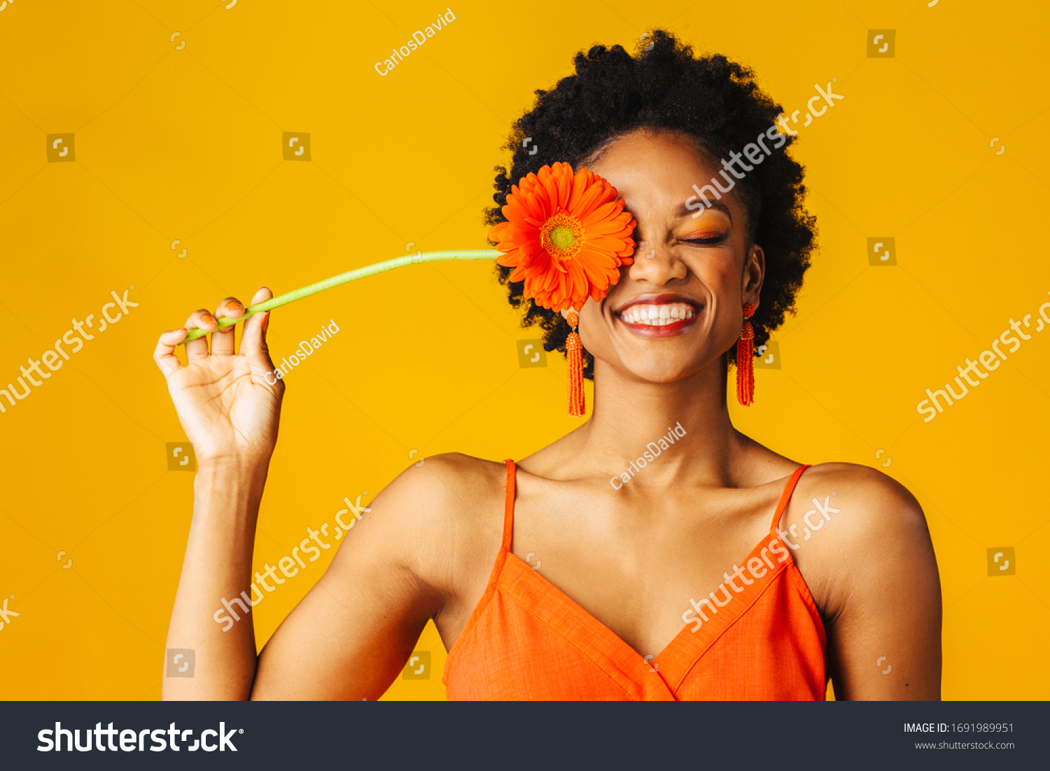 Portrait of a happy young woman holding orange Gerbera daisy covering her eye with eyes closed #1691989951
