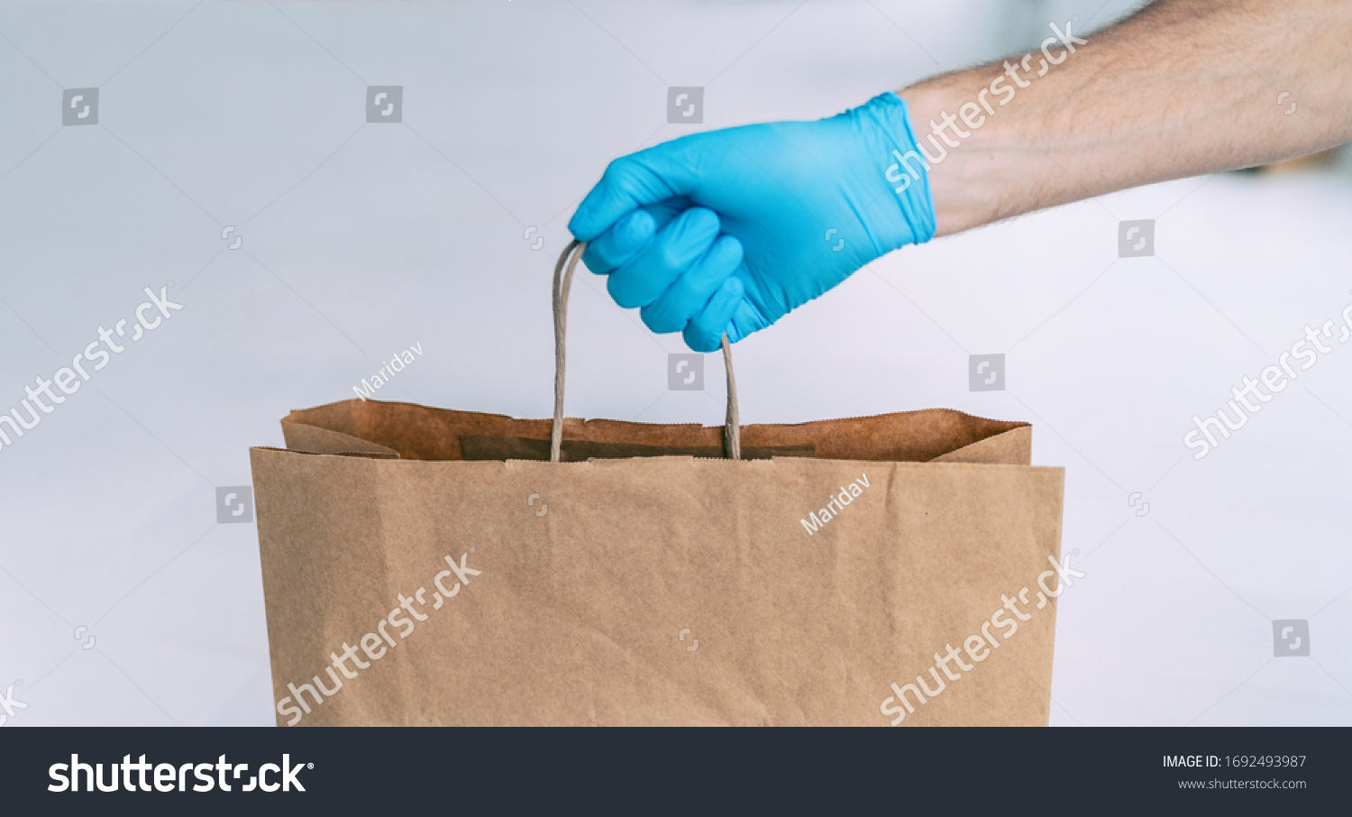 Grocery store shopping delivery man giving paper bag wearing blue glove as protection for COVID-19 Coronavirus precautions. #1692493987