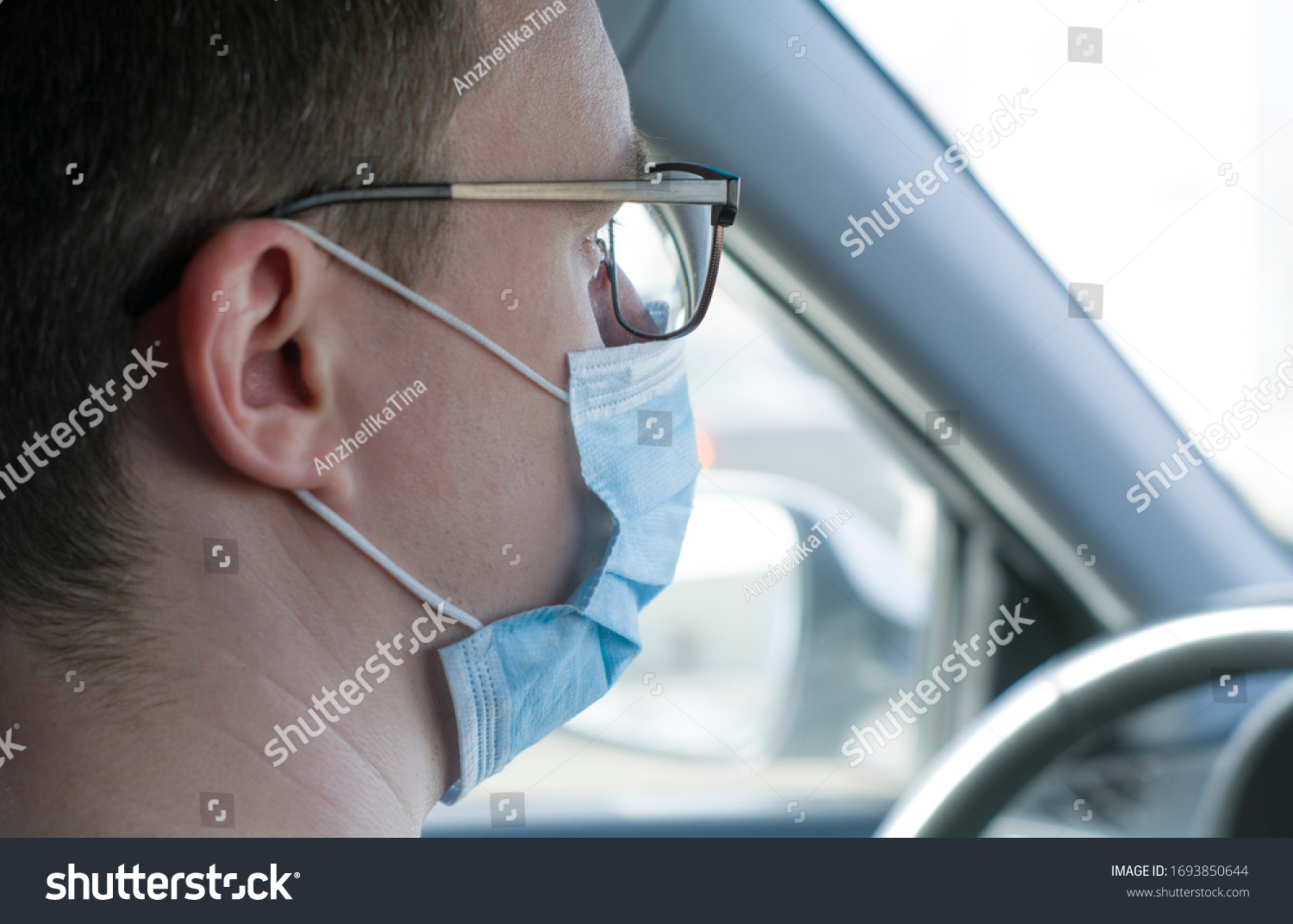 Coronavirus. a young male driver is sitting in a car wearing a medical mask. view from the back seat of the car. self-defense against the virus #1693850644