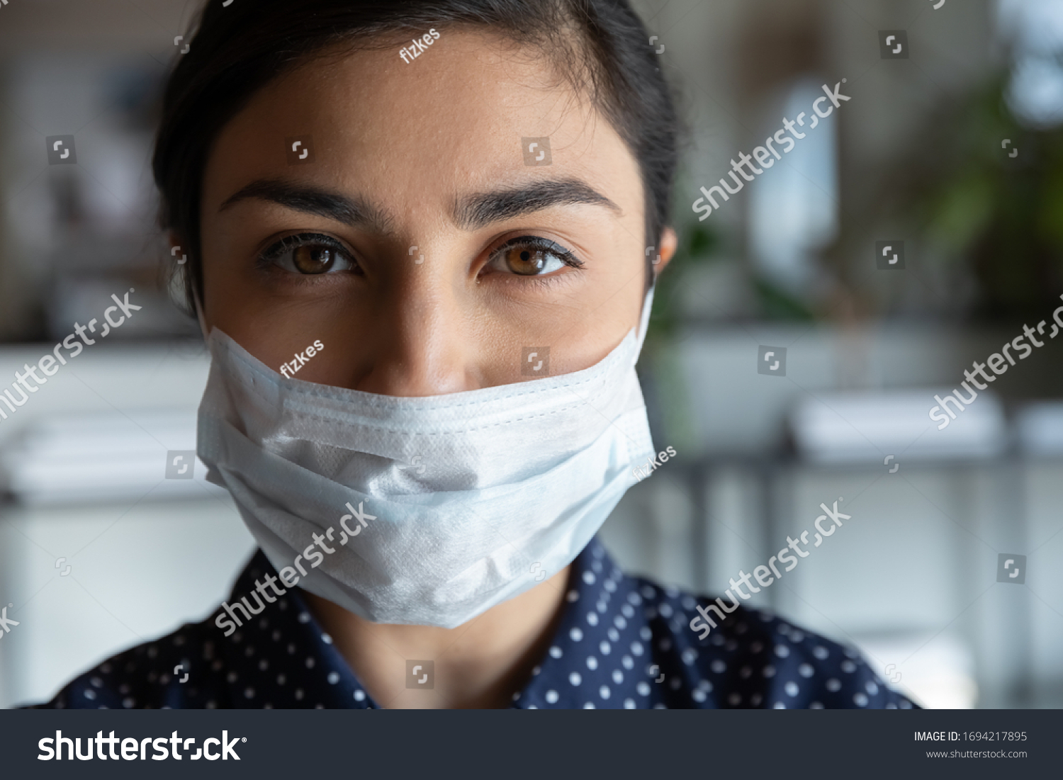Close up head shot portrait young serious cautious indian ethnic woman employee worker wearing protective medical mask, looking at camera, keeping corporate quarantine rules, healthcare concept. #1694217895