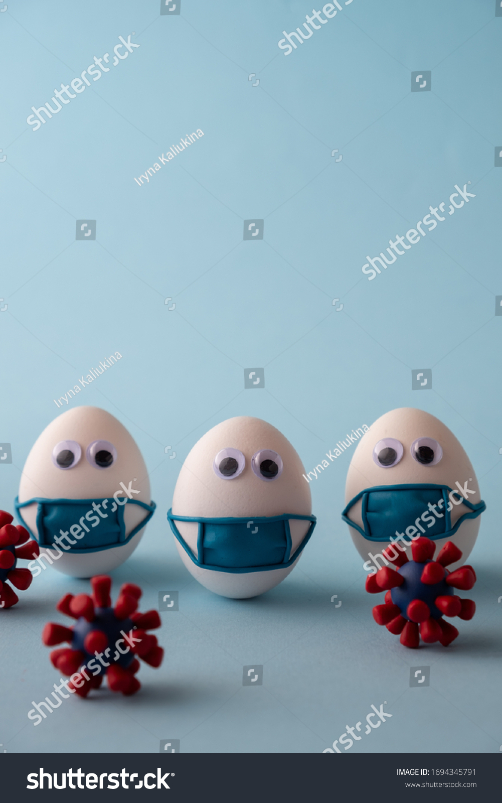 Eggs wearing medical mask for stop coronavirus and models of covid-19 virus on blue background. Epidemic coronavirus COVID-19 concept. Place fo text #1694345791